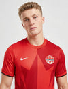 Maglia Canada Home 2026 Nike, close-up busto: dettaglio della grafica a stella in rosso scuro su fondo rosso, stemma Canada Soccer cucito con scritta CANADA, swoosh Nike bianco, texture a costine verticali del tessuto Dri-FIT, colletto a V con bordino rosso scuro