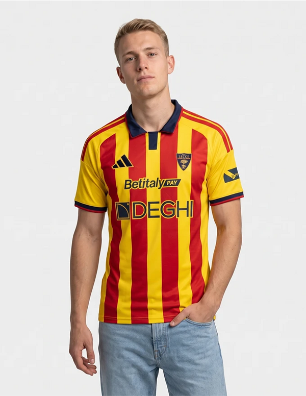 Maglia Lecce Home 2026/2027 Adidas gialla e rossa a righe con collo blu indossata a figura intera